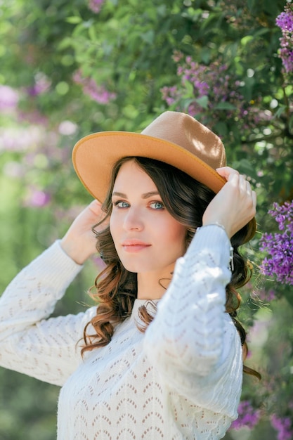 Portret van mooie jonge darkhaired vrouw met blauwe ogen in hoed dichtbij het bloeiende Gelukkige model met krullend haar De lente