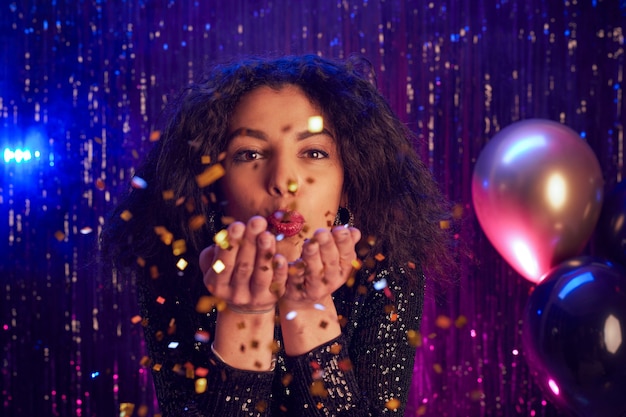 Foto portret van mooie jonge vrouw blazen glitter op camera close-up terwijl u geniet van feest in nachtclub, kopieer ruimte