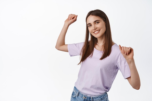 Portret van mooie jonge vrouw dansen, handen vrij en ontspannen opsteken, lachende witte tanden, genieten van de zomer, feesten, staande tegen een witte achtergrond