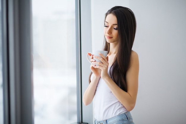 Portret van mooie jonge vrouw die bij het raam staat