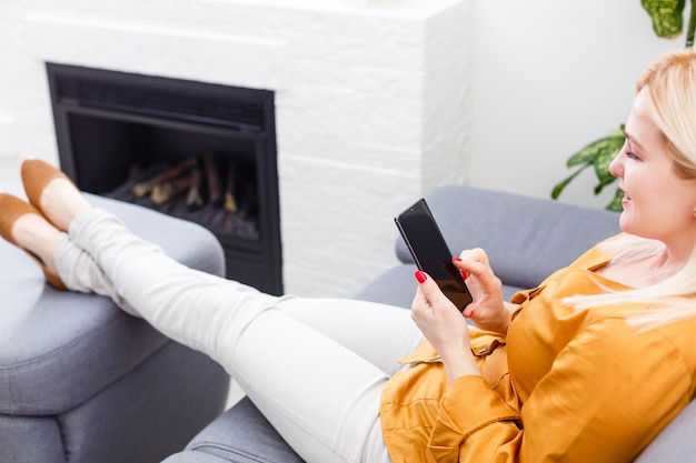 Portret van mooie jonge vrouw die haar mobiele telefoon thuis met behulp van.