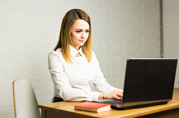 Portret van mooie jonge vrouw die met laptop in haar bureau werkt.