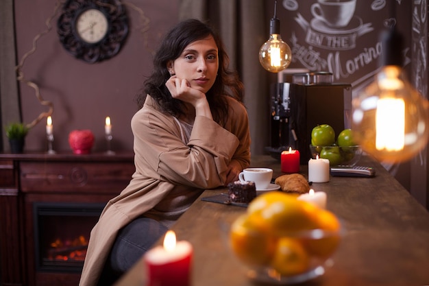 Portret van mooie jonge vrouw die naar de camera kijkt en aan de bar zit in een elengat-koffieshop. Schitterende Kaukasische jonge vrouw in een koffiewinkel.