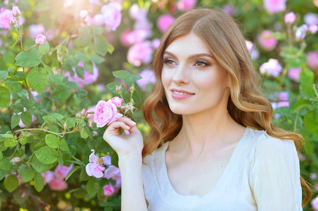 Portret van mooie jonge vrouw die zich voordeed bij rozenstruik