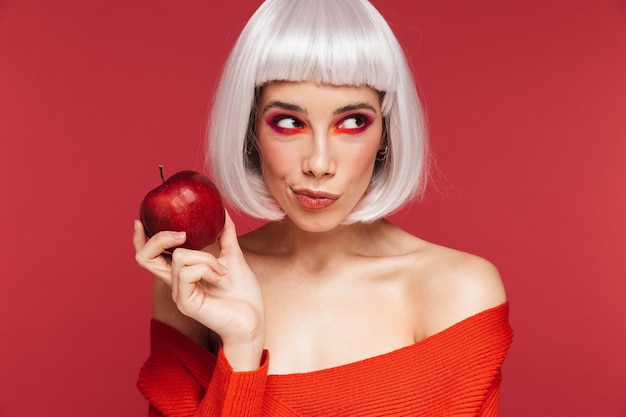 Portret van mooie jonge vrouw geïsoleerd op rode muur met appel.
