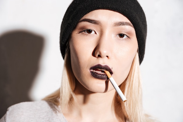 Portret van mooie jonge vrouw hipster in hoeden rokende sigaret