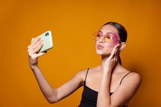 Portret van mooie jonge vrouw kijkt naar de telefoon, heldere make-up poseren mode emoties gele achtergrond ongewijzigd