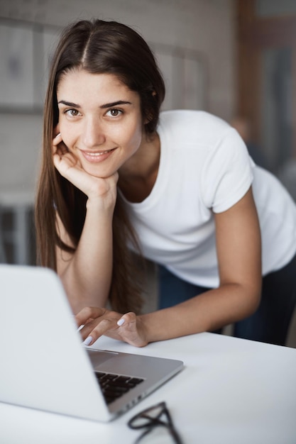 Portret van mooie jonge vrouw met behulp van laptopcomputer in studioruimte kijken camera glimlachend