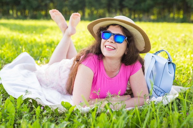 Portret van mooie jonge vrouw met hoed en zonnebril liggend in het park op picknick