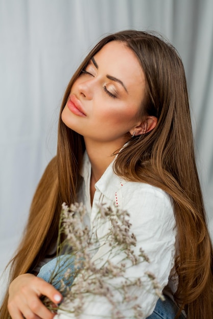 Portret van mooie jonge vrouw met lang haar op witte achtergrond met gedroogde bloemen Lente