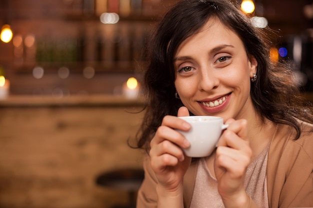 Portret van mooie jonge vrouw ontspannen met een goede koffie en glimlachend in de camera in een coffeeshop. aantrekkelijke vrouw met een aromatische koffie.