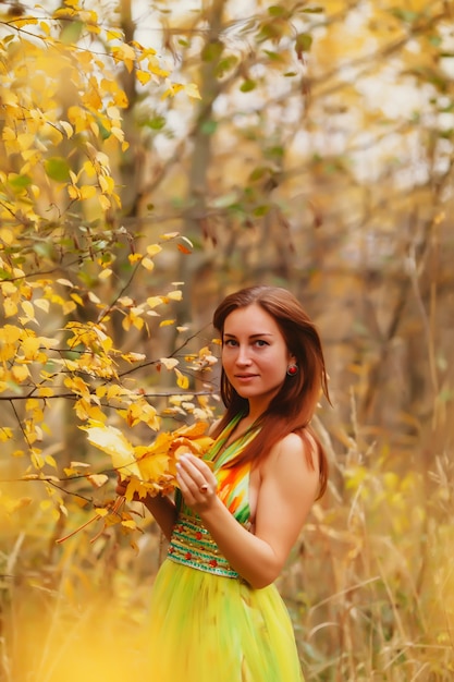 Portret van mooie jonge vrouw van Slavische verschijning in geel gekleurde jurk in de herfst, wandeling in het bos. Schattig model loopt in het park in de gouden herfst tegen de achtergrond van de natuur