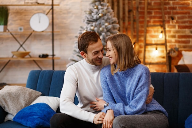 Portret van mooie lachende paar knuffelen op kerstavond. Mooie jonge paar thuis genieten van tijd samen doorbrengen. Wintervakantie, kerstvieringen, nieuwjaarsconcept.