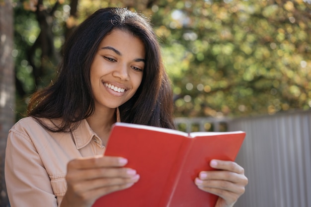 Portret van mooie lachende vrouw leesboek close-up, studeren, taal leren, zittend in het park