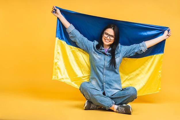 Portret van mooie mooie mooie blij vrolijke vrouw in handen Oekraïense vlag met plezier geïsoleerd over gele pastel kleur achtergrond zittend op de vloer in lotus houding