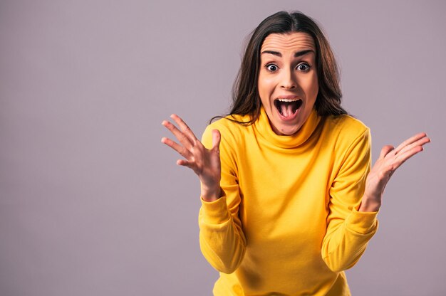 Portret van mooie opgewonden gelukkige jonge brunette vrouw in geel geïsoleerd op een grijze achtergrond