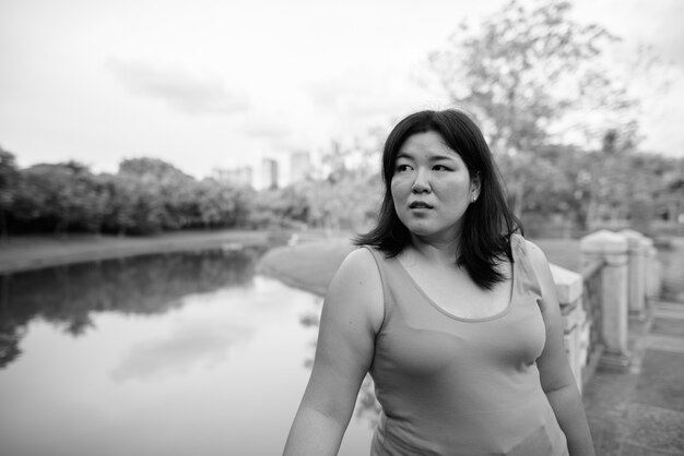 Portret van mooie overgewicht Aziatische vrouw ontspannen in het park in de stad in zwart-wit
