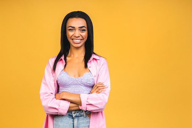 Portret van mooie positieve Afro-Amerikaanse zwarte vrouw die staat met gekruiste armen geïsoleerd over gele achtergrond