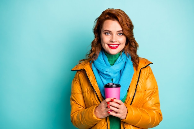 Portret van mooie reiziger dame houden warme koffie drinken handen vrije tijd in het buitenland dragen casual gele overjas sjaal groene coltrui.