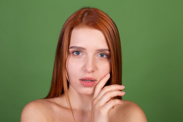 Portret van mooie rode haar jonge vrouw met gladde natuurlijke zachte huid met blote schouders op groene muur, schoonheidsconcept