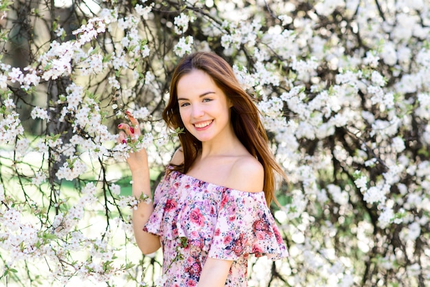 Portret van mooie roodharige jonge vrouw in witte jurk in Lentebloemen, bloesem