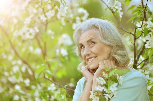 Portret van mooie senior vrouw poseren in de buurt van bloeiende boom