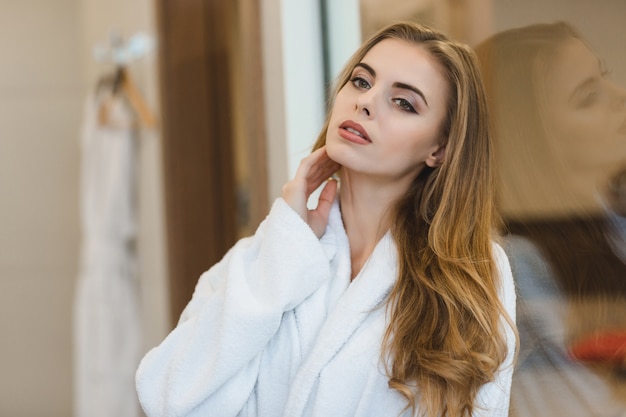 Portret van mooie sensuele jonge blonde vrouw in badjas staande in de badkamer