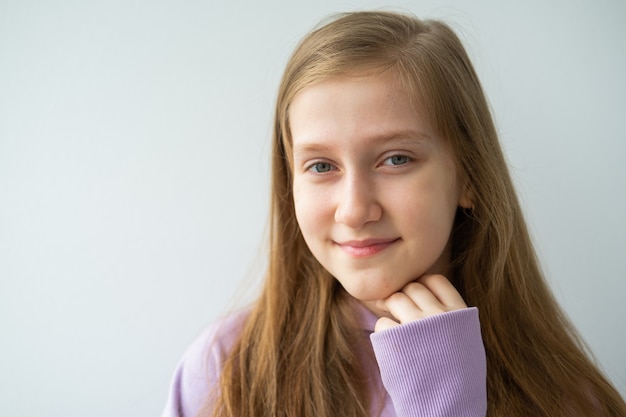 Portret van mooie tiener met lang haar in paarse hoodie staande tegen een witte muur