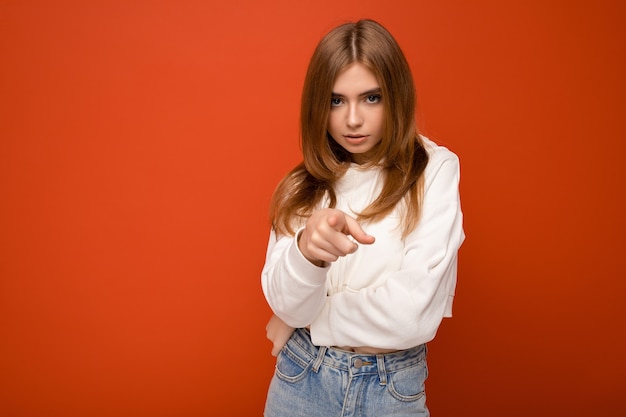 Portret van mooie triest boos bedroefd jonge brunette vrouw, gekleed in gebreide trui geïsoleerd op rode achtergrond met kopie ruimte en kort bruin haar aan te raken en gespleten haarpunten te hebben.