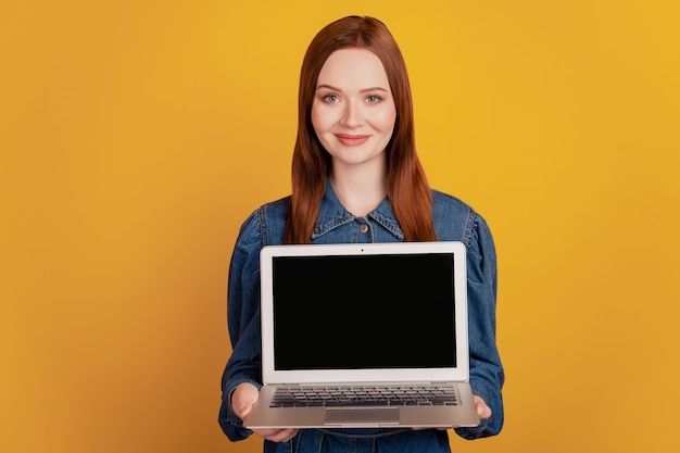 Portret van mooie, vrij betrouwbare dame houdt laptop touchscreen lege ruimte op gele achtergrond