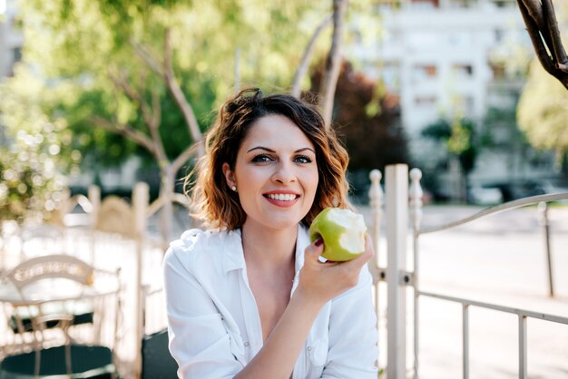 Portret van mooie vrouw die appel in koffie eet openlucht.