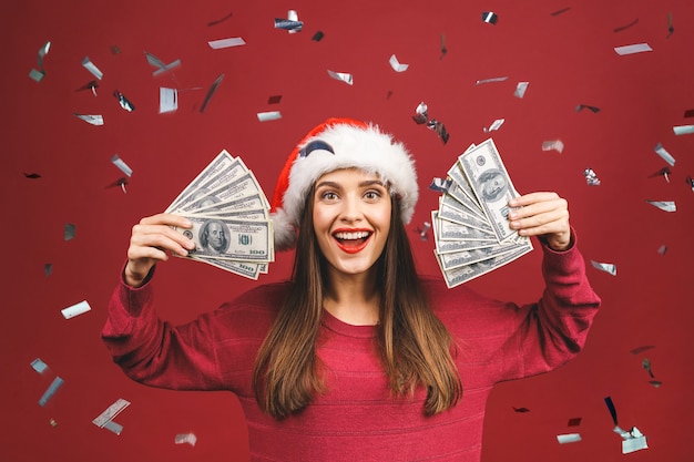 Portret van mooie vrouw die Kerstmanhoed draagt en dollarbankbiljetten houdt