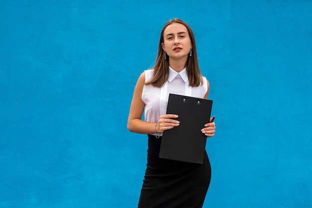 Portret van mooie vrouw in zakelijke kleding met klembord schrijven, geïsoleerd op blue