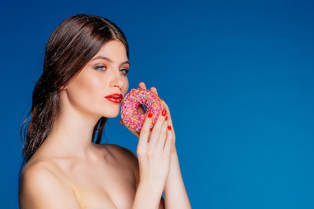 Portret van mooie vrouw met doughnut die op blauwe achtergrond wordt geïsoleerd