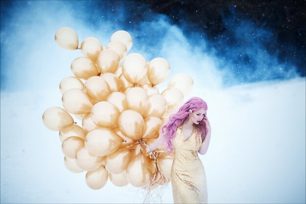 Foto portret van mooie vrouw met roze haar in gouden modieuze lange jurk met kapsel