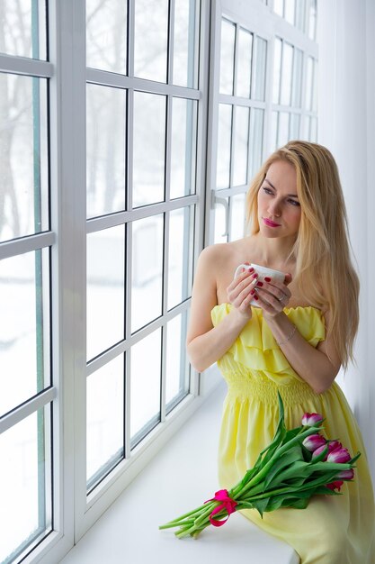 Portret van mooie vrouw met tulpenboeket en kopje thee