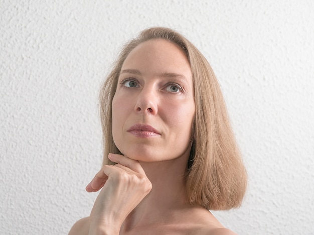 Portret van mooie vrouw van middelbare leeftijd aanraken van haar gezicht op witte muur