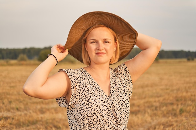 Portret van mooie witte Europese vrouw in jurk en hoed 's avonds buitenshuis?