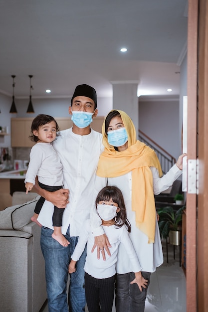 Portret van moslimfamilie die met masker voor hun gastvrije gast thuis tijdens eid Mubarak-viering staan