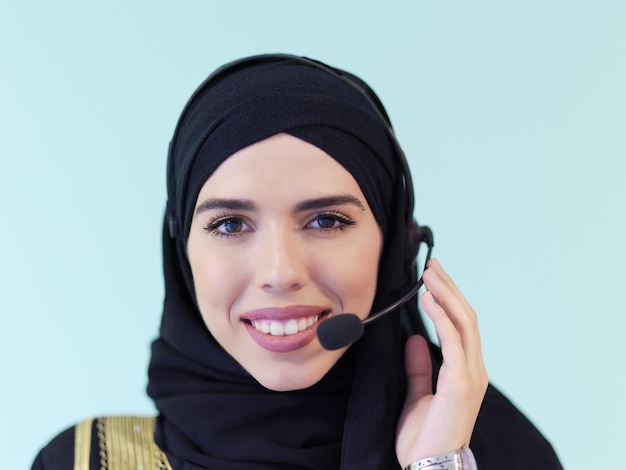 Foto portret van moslimvrouw met hijab-sjaal klantvertegenwoordiger zakenvrouw met telefoonheadset online helpen en ondersteunen met klant in modern callcenter geïsoleerd op cyaanachtergrond
