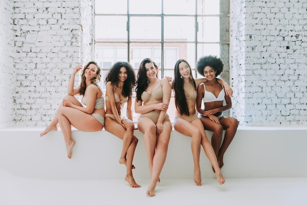 Portret van multi-etnische vrouwen in lingerie die op een steunmuur zitten