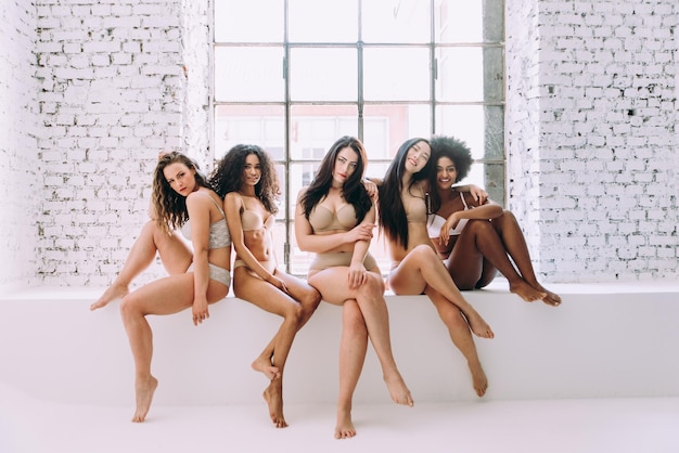 Portret van multi-etnische vrouwen in lingerie die op een steunmuur zitten