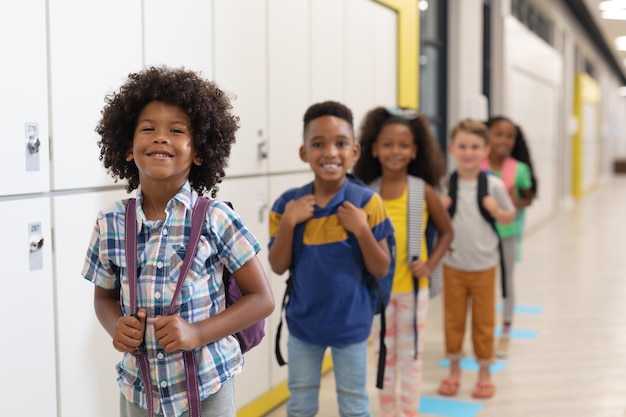 Foto portret van multiraciale lachende basisschoolkinderen met rugzakken die in de rij staan