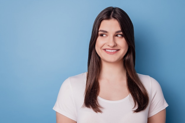 Portret van nieuwsgierige mooie dame ziet er leeg uit, witte stralende glimlach op blauwe achtergrond