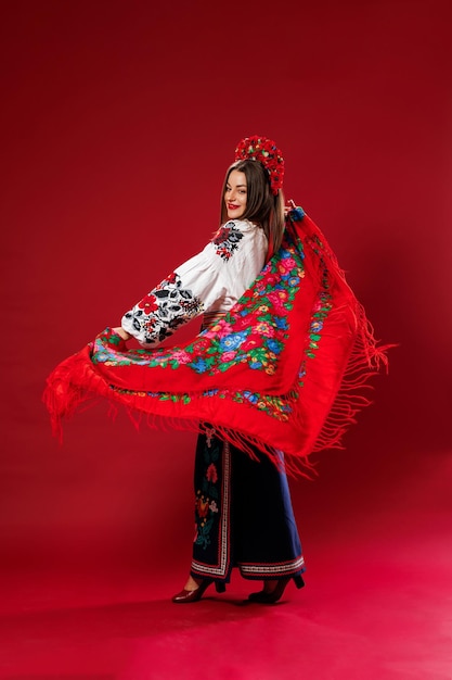 Portret van Oekraïense vrouw in traditionele etnische kleding en bloemen rode krans op viva magenta studio achtergrond draait een zakdoek Oekraïense nationale geborduurde jurk oproep vyshyvanka