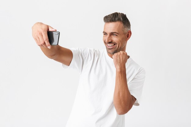 Portret van ongeschoren man 30s dragen casual t-shirt nemen selfie geïsoleerd op wit