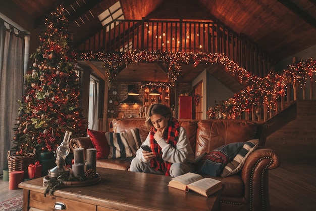 Portret van openhartige authentieke glimlachende knappe jongenstiener die mobiele telefoon gebruikt in het interieur van Xmas