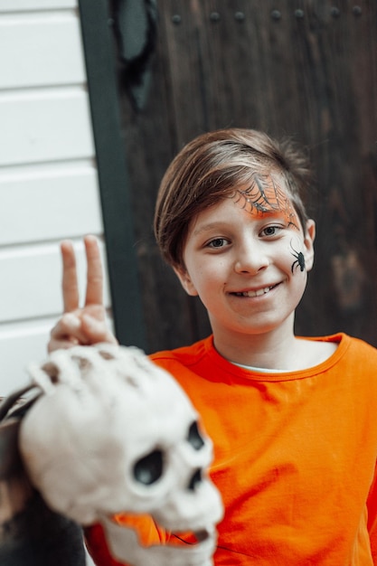 Portret van openhartige authentieke tienerjongen met beschilderd gezicht op versierd skeletfeest Halloween