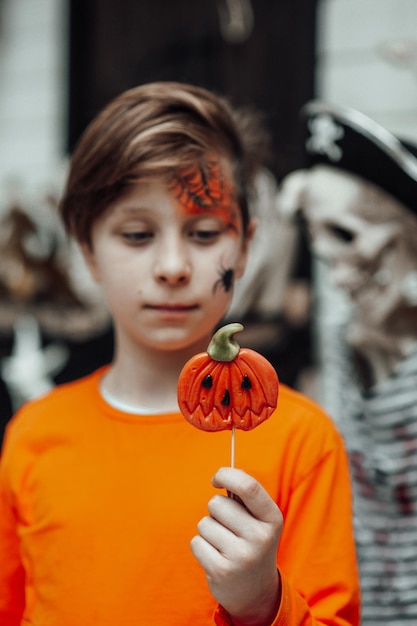 Portret van openhartige authentieke tienerjongen met geschilderd gezicht op feest Halloween met Jack lolly