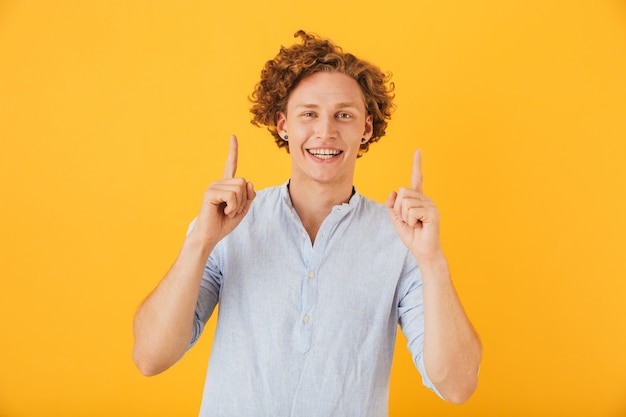 Portret van opgewonden blije man lachen en wijzende vingers omhoog op copyspace, geïsoleerd op gele achtergrond